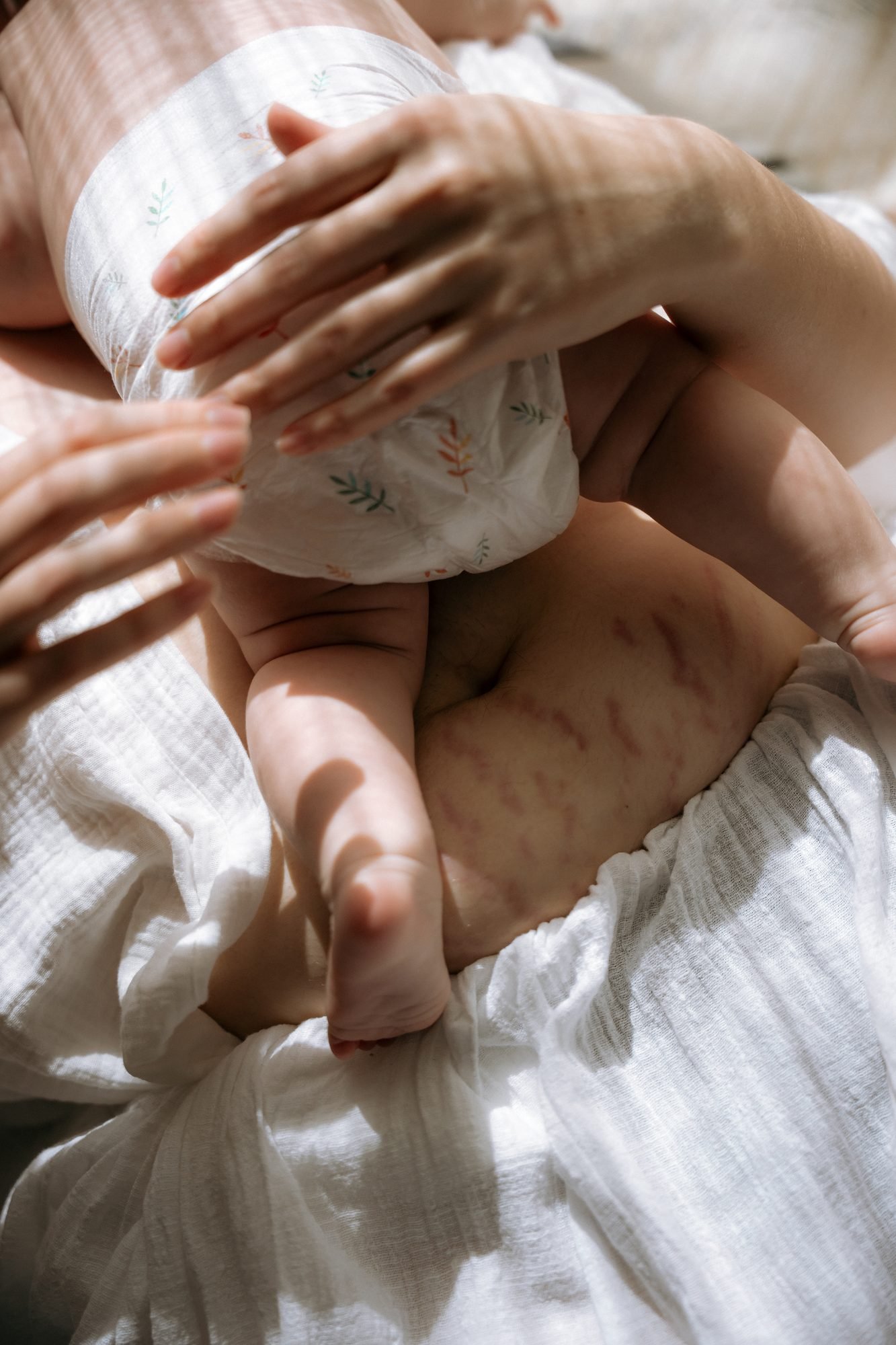 Mains d'une mère autour d'un bébé emmailloté, marques douces sur la peau