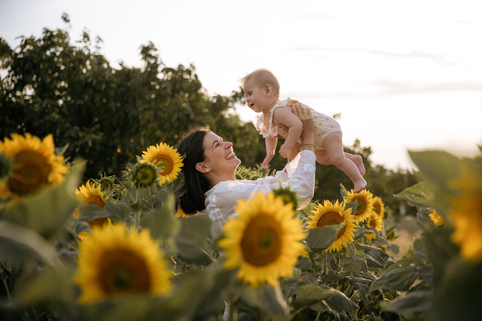 Bébé levé vers le ciel avec un grand sourire, champ de tournesols