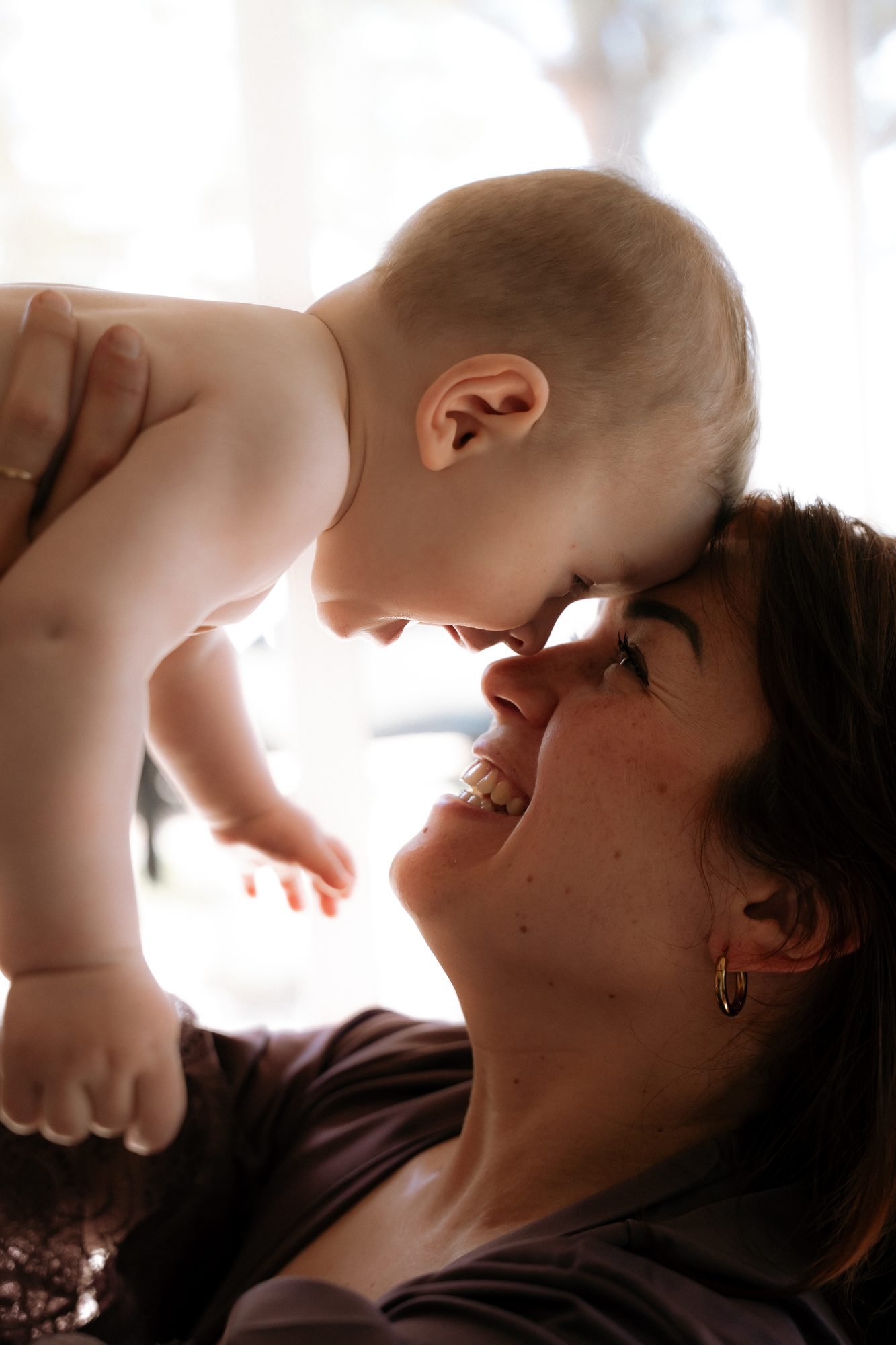 Mère riant en portant son bébé au-dessus d'elle, à contre-jour
