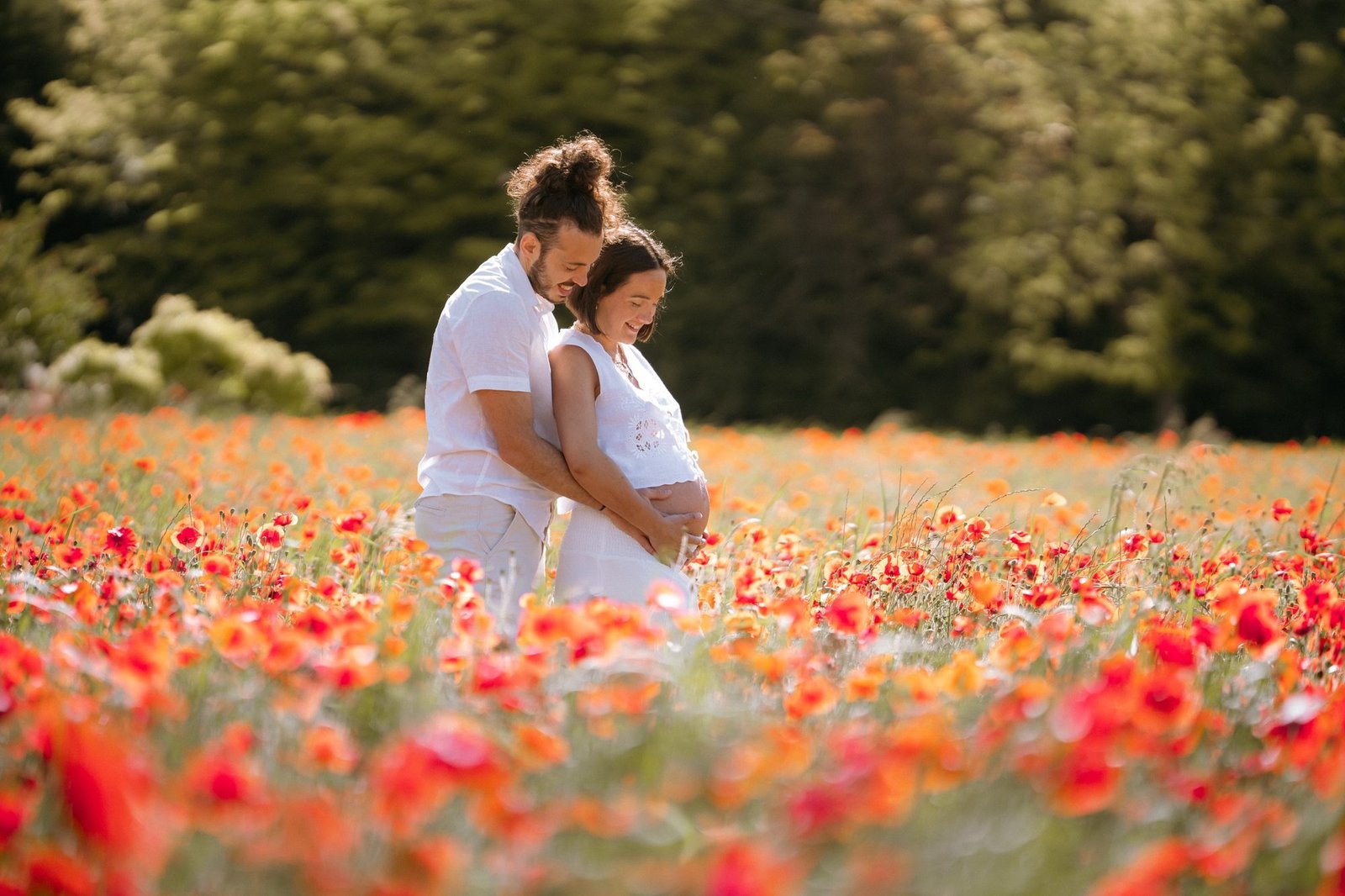 Couple enlacé et souriant dans un champ de coquelicots, femme enceinte