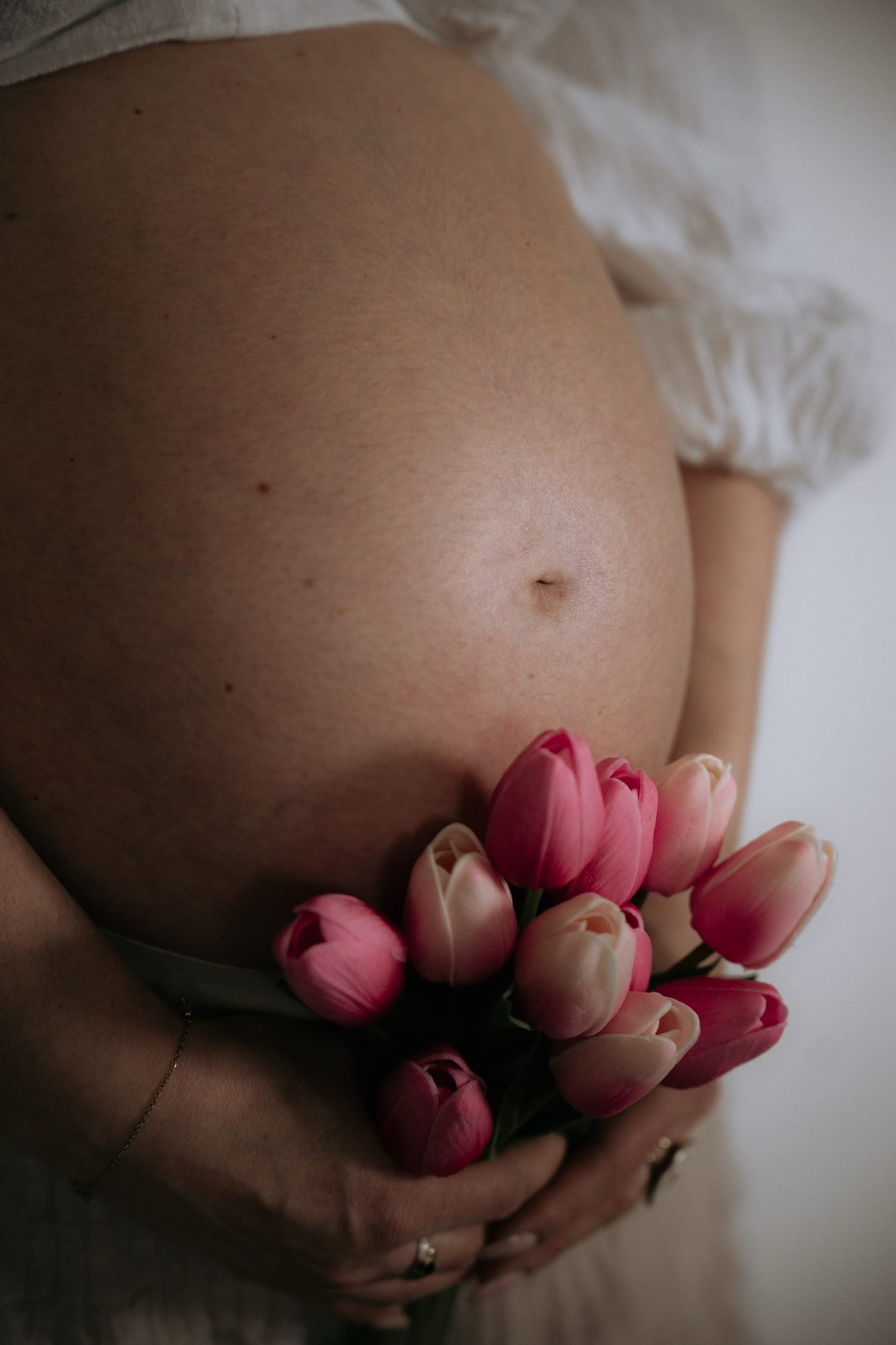 Femme enceinte souriante avec un chat sur le ventre, fleurs roses