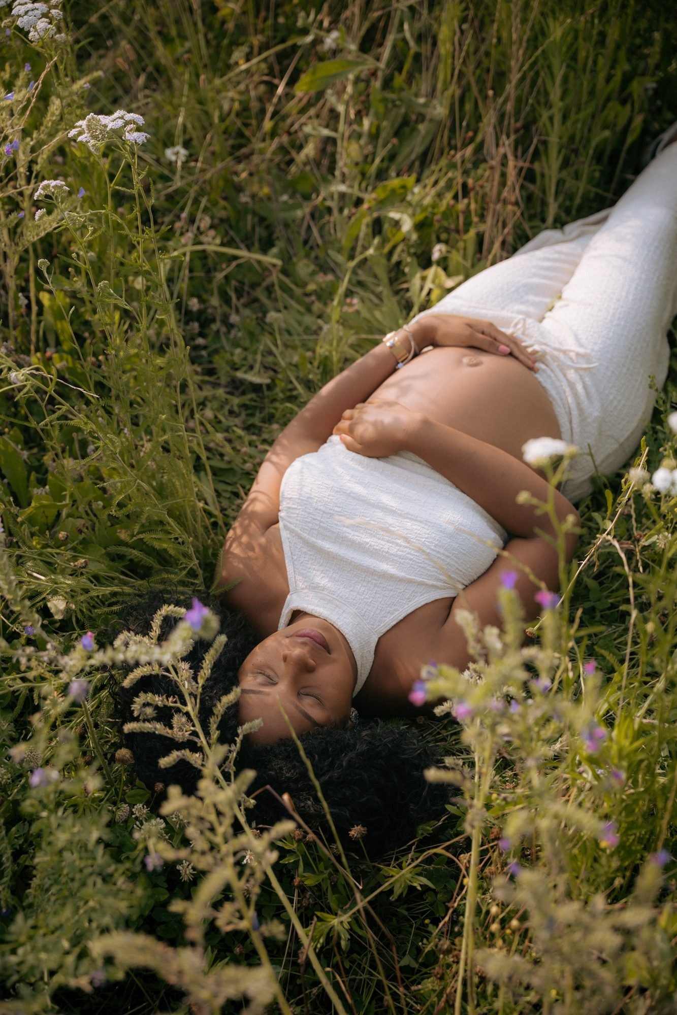 Femme enceinte souriante allongée dans l'herbe, tenue blanche