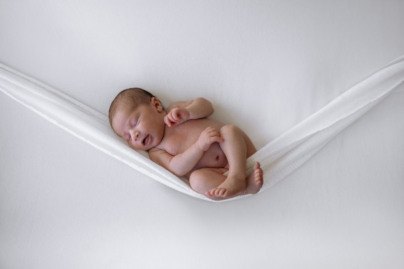Nouveau-né souriant dans un hamac en tissu blanc, bras levé