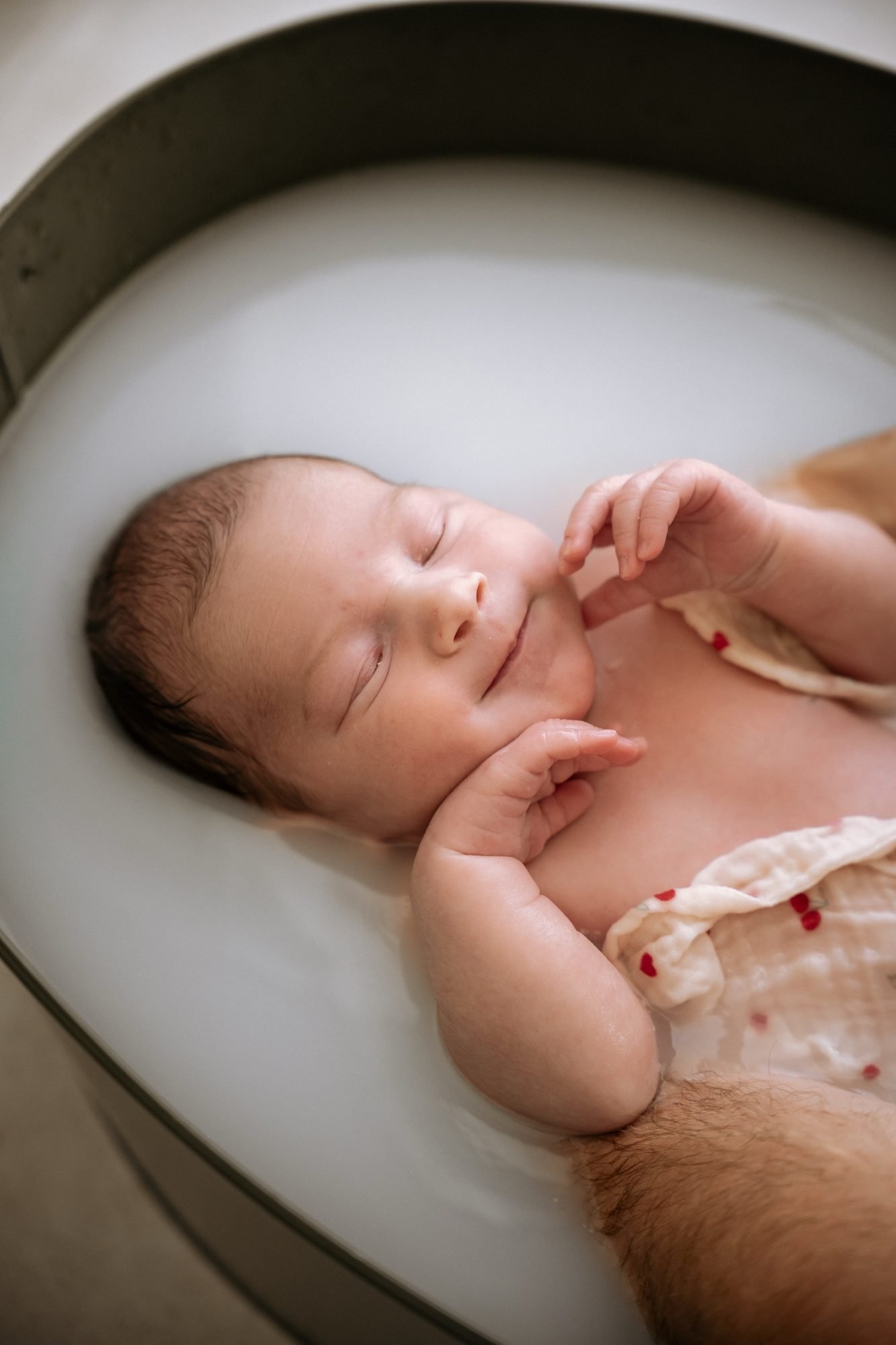 Nouveau-né souriant dans son bain, doudou brodé de cœurs