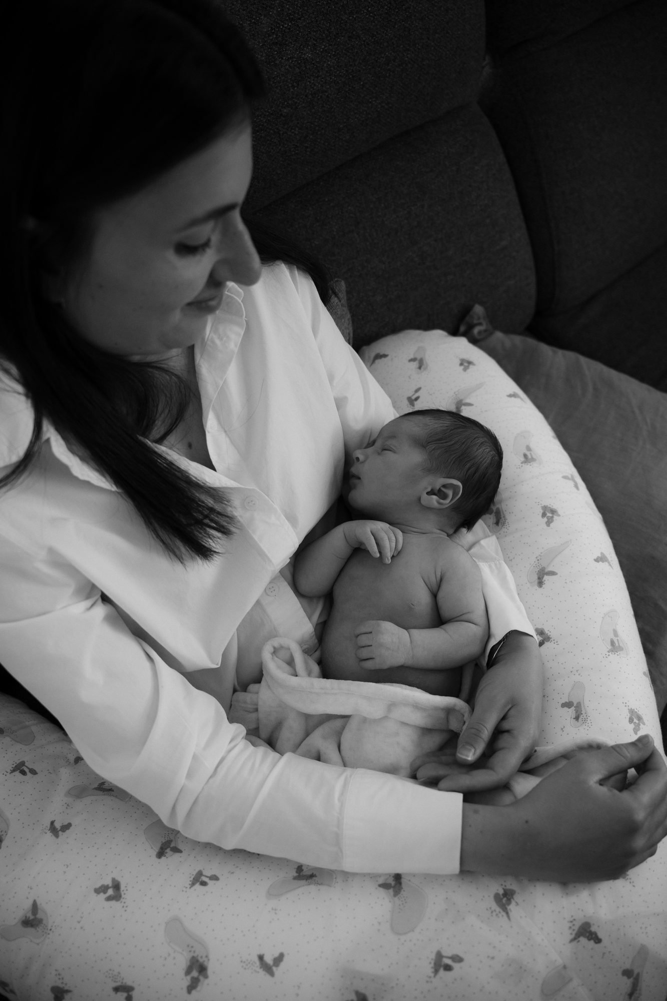 Mère regardant son nouveau-né endormi sur un coussin d'allaitement, noir et blanc
